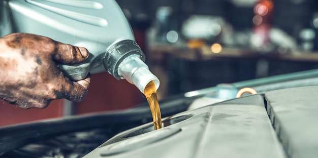 Mano recortada de un mecánico vertiendo aceite de motor en un vehículo