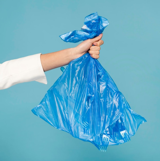 Mano recortada de una mujer sosteniendo una bolsa de plástico contra un fondo azul