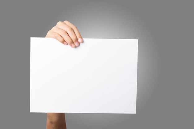 Foto mano recortada de una mujer sosteniendo un papel en blanco contra un fondo gris