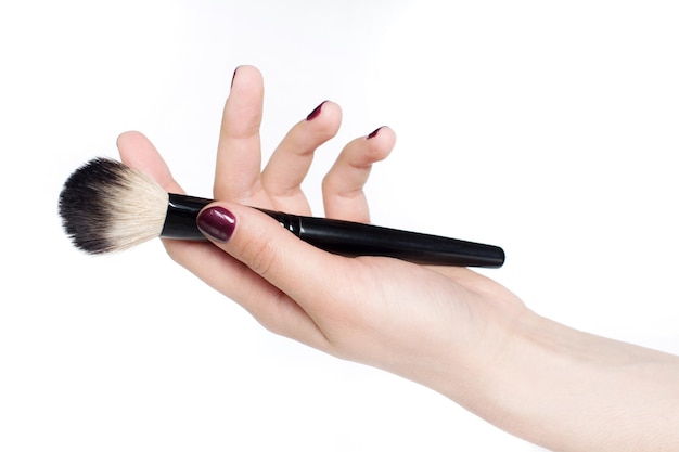 Mano recortada de una mujer sosteniendo un pincel de maquillaje contra un fondo blanco