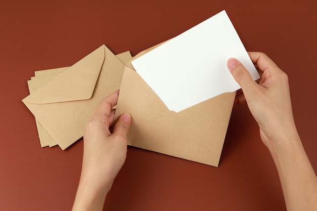 Foto mano recortada de una mujer sosteniendo un sobre con papel sobre fondo marrón