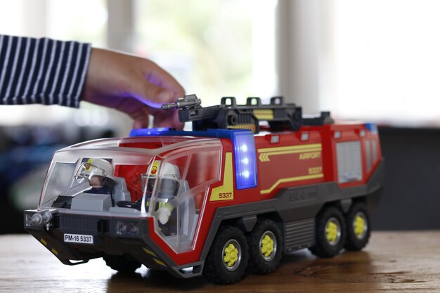 Foto mano recortada de un niño jugando con un motor de bomberos de juguete en la mesa