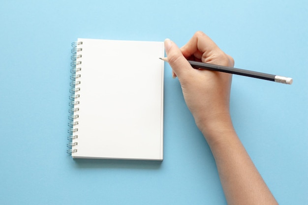 Mano recortada de una persona escribiendo en un libro contra un fondo azul