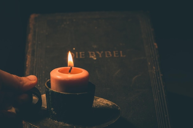 Mano recortada de una persona que sostiene un candelabro encendido por el cuarto oscuro de la Biblia