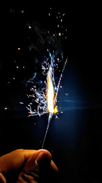 Mano recortada de una persona que sostiene una chispa iluminada por la noche