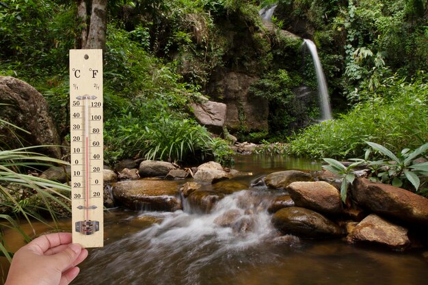 Foto mano recortada de una persona que sostiene un termómetro junto a una cascada