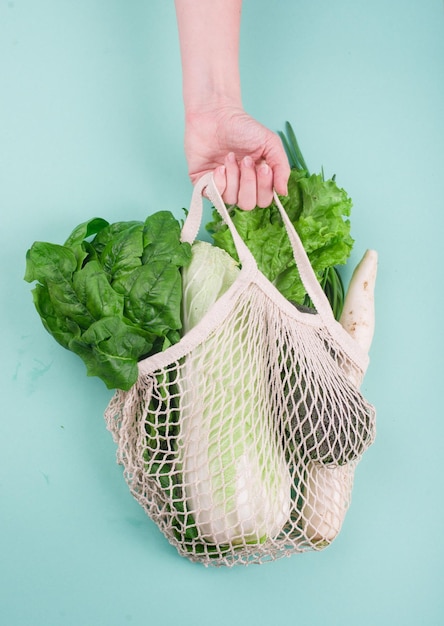 Mano recortada de una persona sosteniendo una canasta de verduras contra un fondo azul