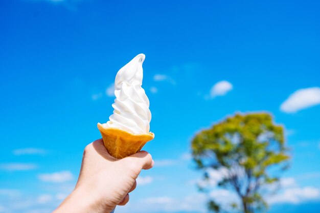 Mano recortada de una persona sosteniendo un cono de helado contra el cielo azul