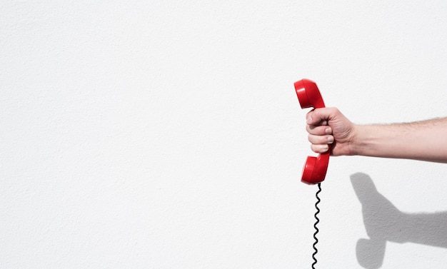 Foto mano recortada de una persona sosteniendo un teléfono rojo contra la pared