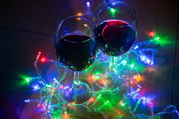 Mano recortada que sostiene la copa de vino sobre coloridas luces de Navidad iluminadas en el cuarto oscuro