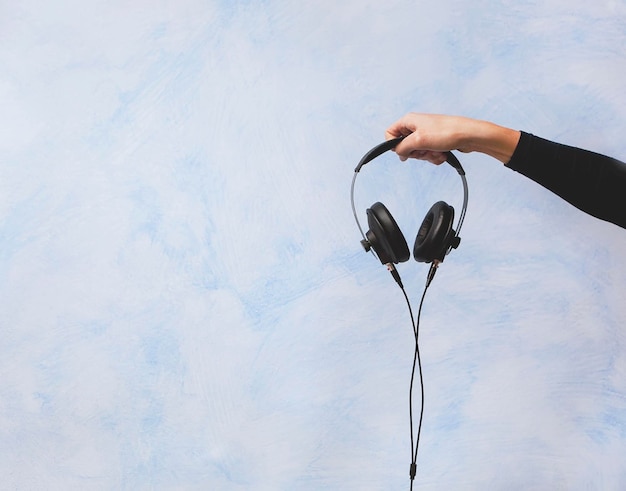 Foto mano recortada sosteniendo auriculares contra la pared