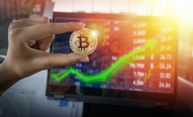 Mano recortada sosteniendo bitcoin con una computadora portátil