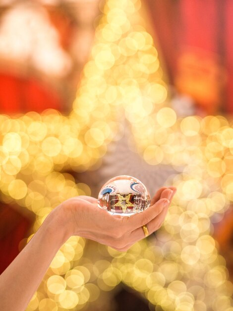 Foto mano recortada sosteniendo una bola de cristal contra una decoración navideña en forma de estrella iluminada