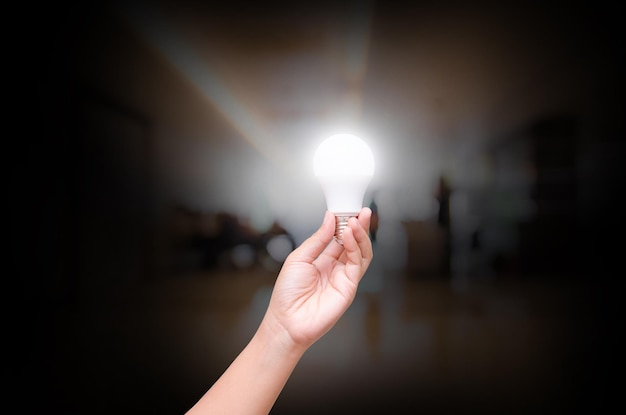 Foto mano recortada sosteniendo una bombilla iluminada en el cuarto oscuro