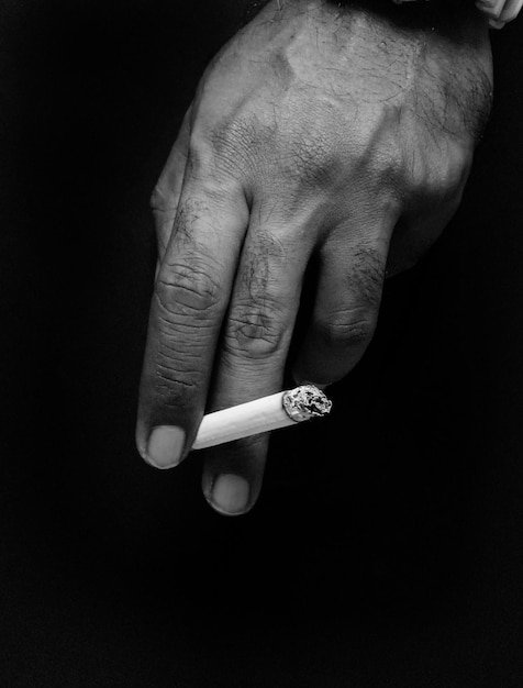 Foto mano recortada sosteniendo un cigarrillo contra un fondo negro