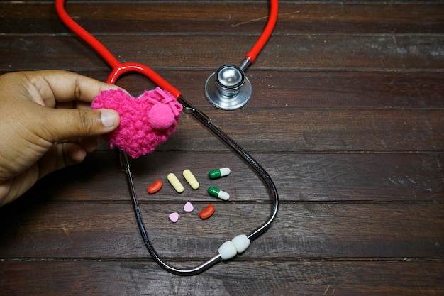 Foto mano recortada sosteniendo la forma de un corazón sobre la mesa con estetoscopio y pastillas de medicina