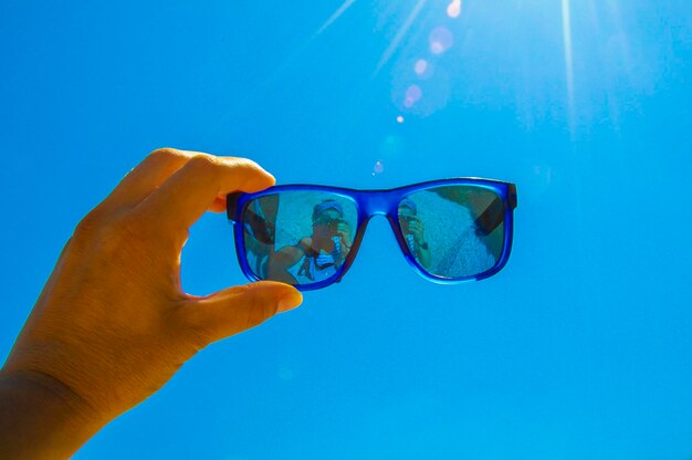 Mano recortada sosteniendo gafas de sol contra el cielo azul claro durante un día soleado