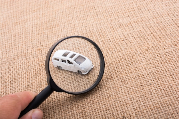 Mano recortada sosteniendo una lupa por un coche de juguete en burlap