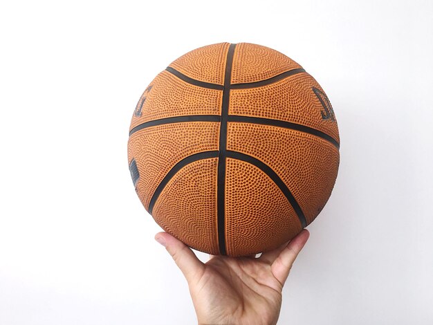 Foto mano recortada sosteniendo una pelota de baloncesto contra un fondo blanco