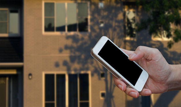 Mano recortada sosteniendo un teléfono móvil contra el edificio