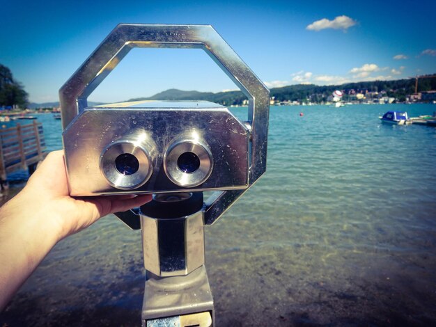 Mano recortada tocando un binocular con moneda en la playa en un día soleado