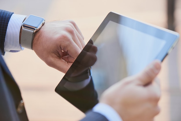 Mano con reloj inteligente y una mano sosteniendo la tableta