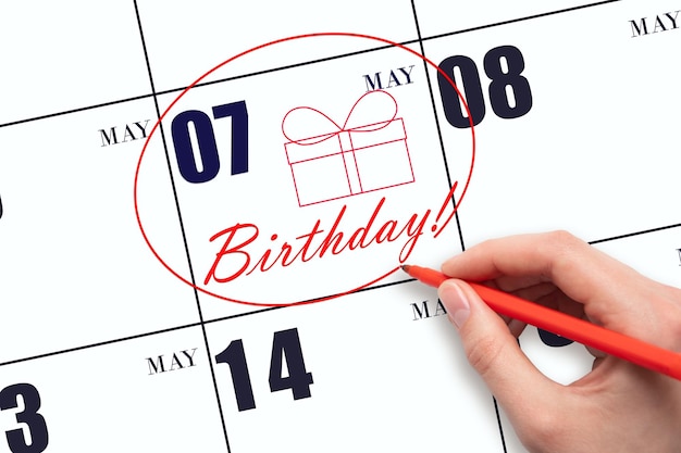 La mano rodea la fecha en el calendario 7 de mayo dibuja una caja de regalo y escribe el texto Fiesta de cumpleaños