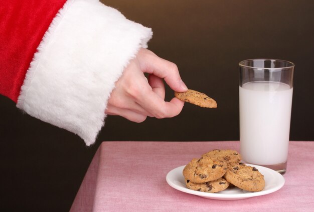 Mano de Santa Claus con galleta de chocolate sobre fondo marrón