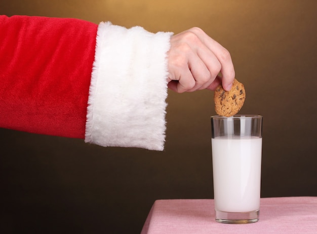 Mano de Santa Claus con galleta de chocolate sobre superficie marrón