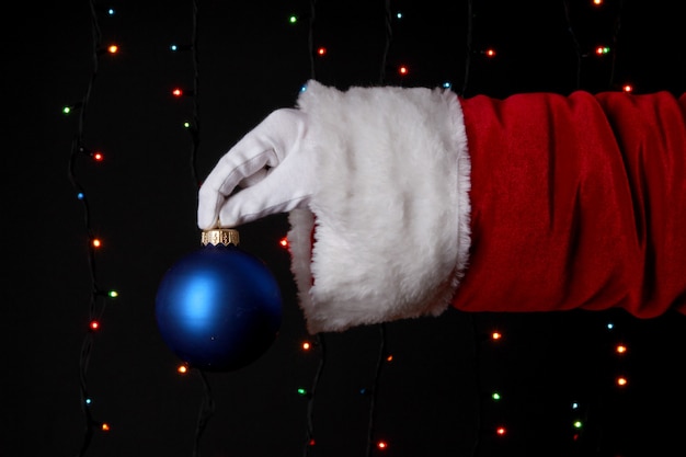 Mano de Santa Claus sosteniendo la bola de Navidad sobre fondo brillante