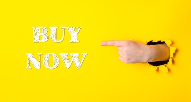 Una mano señalando la palabra comprar ahora en un fondo amarillo