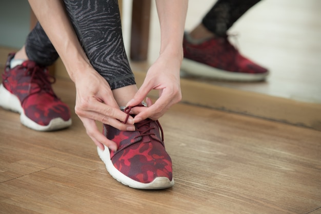 La mano de la señora se puso en las acciones de los cordones del zapato en el gimnasio para el culturista con los zapatos rojos