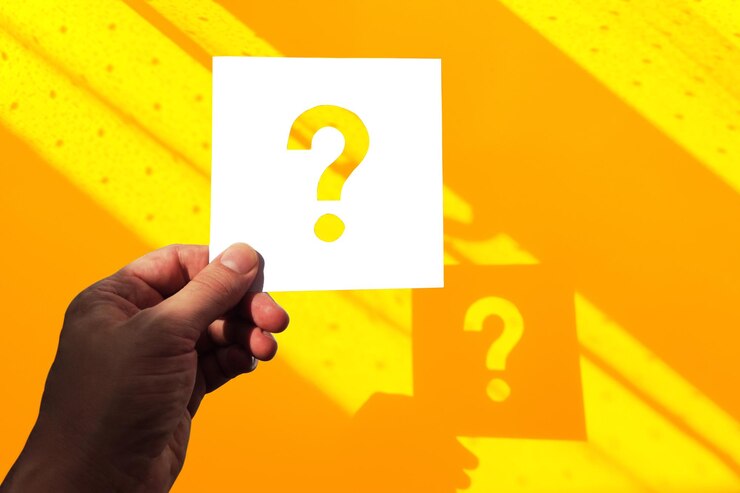 Foto mano con un signo de interrogación en un fondo amarillo