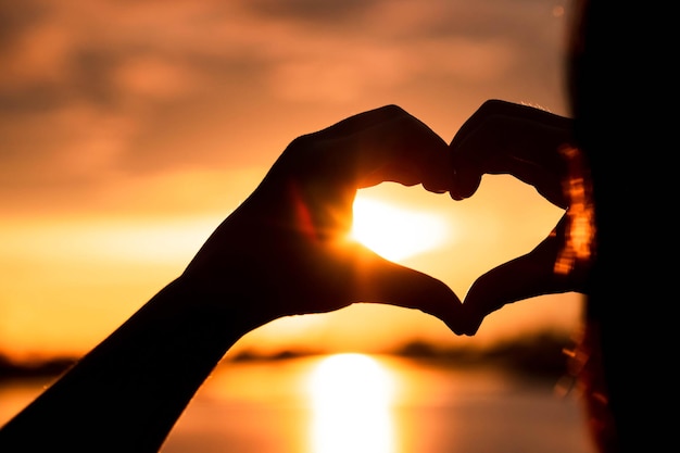 Mano de silueta en forma de corazón con amanecer en el medio y fondo de playa