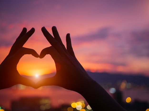 Mano de silueta para ser una forma de corazón durante el atardecer de fondo.