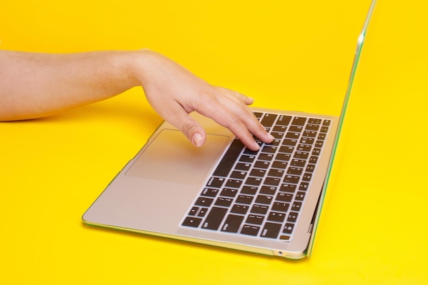 Foto mano sobre el teclado de la computadora portátil sobre un fondo amarillo. concepto de trabajo de forma remota. trabajo independiente