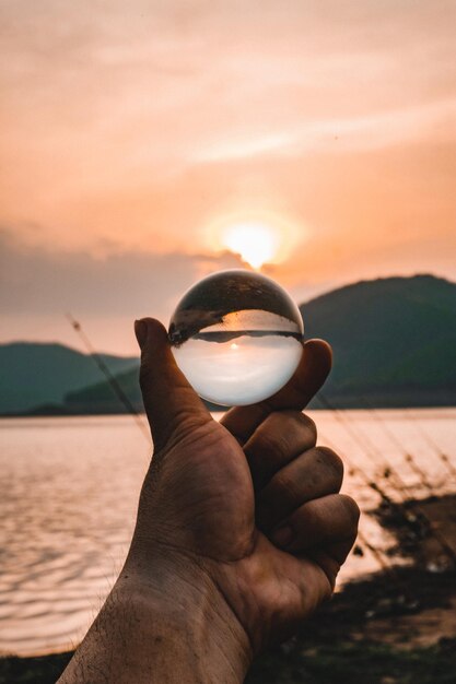 Foto la mano sosteniendo el agua contra el cielo durante la puesta del sol