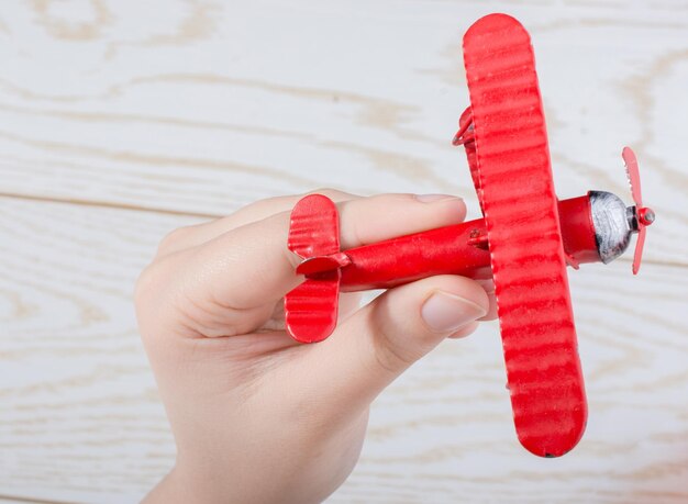 Foto mano sosteniendo un avión de juguete rojo sobre una textura de madera