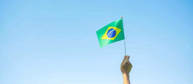 Mano sosteniendo la bandera de Brasil sobre fondo de cielo azul. Septiembre día de la independencia y conceptos de celebración feliz