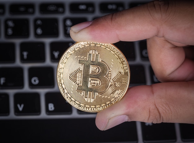 mano sosteniendo bitcoin dorado con la computadora portátil