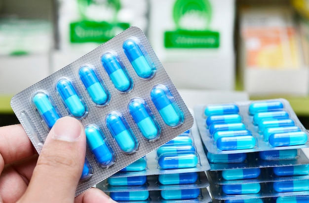 Mano sosteniendo un blister de cápsulas azules en la tienda de farmacia