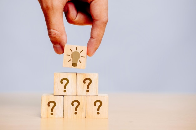Mano sosteniendo un bloque de cubo de madera en el signo de interrogación ¿qué significa en el fondo de la mesa de cemento?