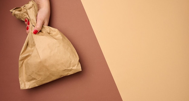 Mano sosteniendo una bolsa de papel llena de papel kraft marrón sobre un fondo marrón de cerca