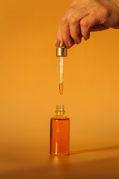 mano sosteniendo una botella de aceite en un frasco de vidrio sobre un fondo amarillo