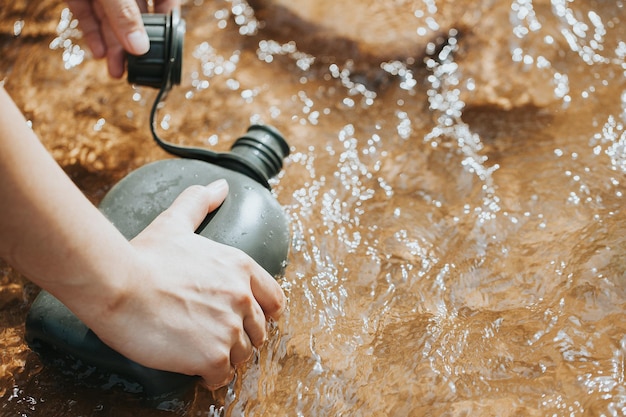 Mano sosteniendo una botella de agua en el arroyo