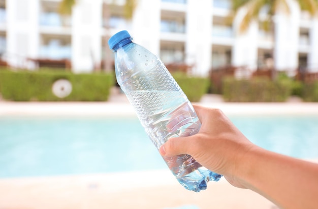 Una mano sosteniendo una botella de agua frente a una piscina