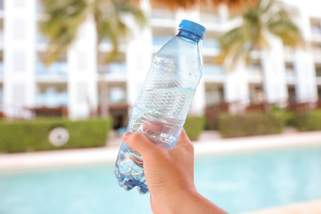 Una mano sosteniendo una botella de agua frente a una piscina