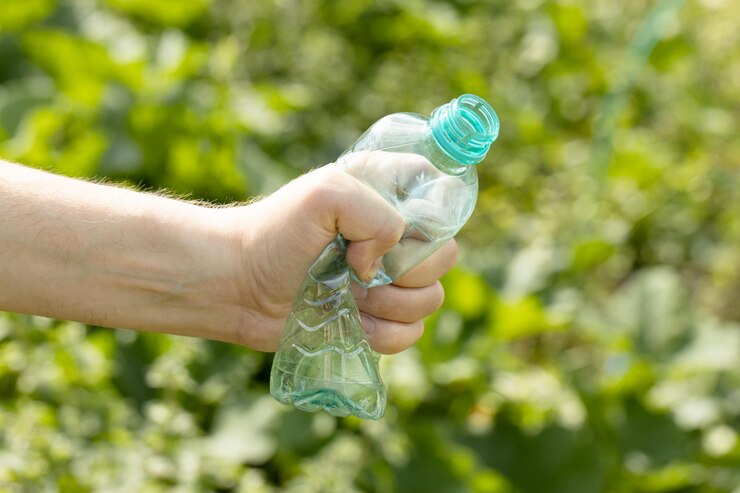Foto la mano sosteniendo una botella de plástico vacía arrugada en el parque