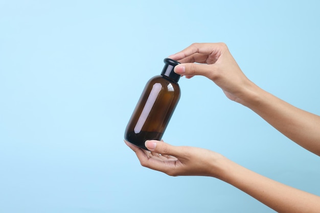 Mano sosteniendo una botella de vidrio transparente marrón aislada sobre un fondo azul