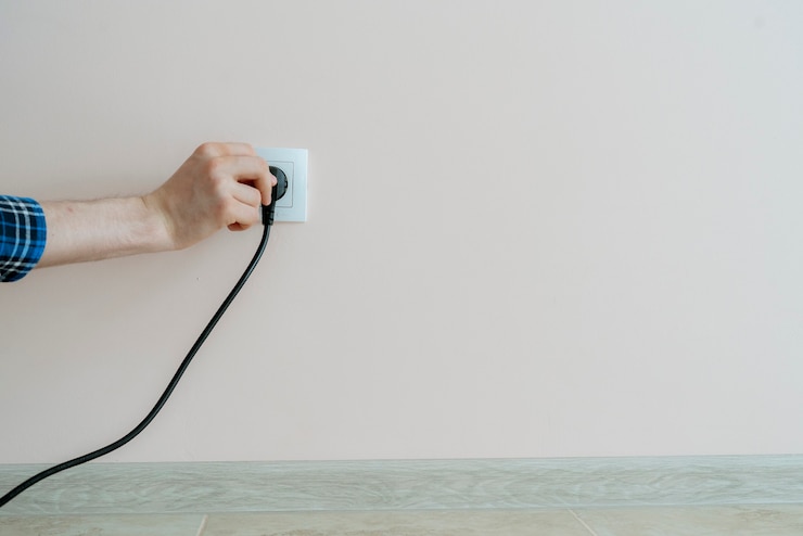 Foto una mano sosteniendo el cable de alimentación eléctrica e insértelo en el enchufe de la pared en casa